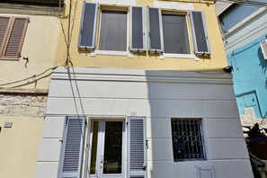 Un edificio con varias ventanas, algunas con contraventanas, y una puerta visible.