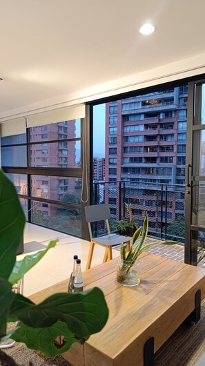 A modern living room with a large window, a wooden dining table, a chair, and a potted plant. - Fresh, Modern, Poblado Loft close to everything! (Medellín)