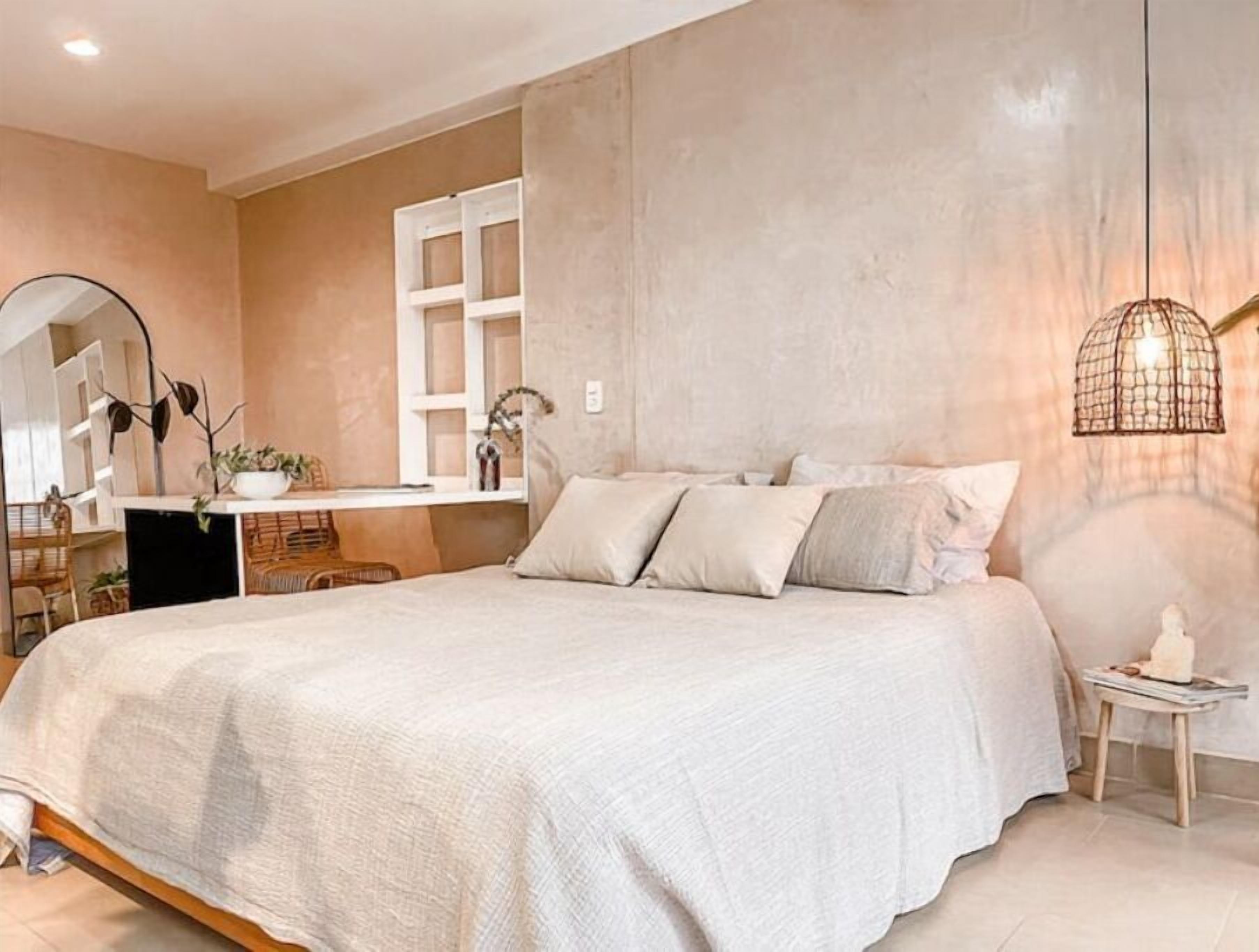 Ein Schlafzimmer mit einem großen Bett, einem Nachttisch, einem Spiegel und einer Pendelleuchte.