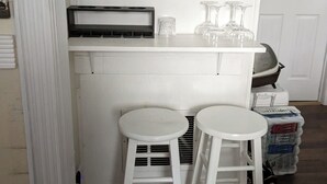 Un petit coin cuisine avec deux tabourets blancs, un plan de travail blanc et une porte blanche en arrière-plan.