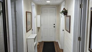 Un couloir avec une porte blanche, un meuble blanc et un paillasson noir.