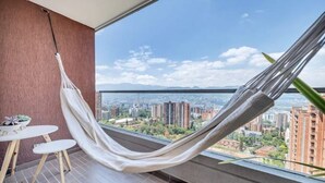 A balcony with a hammock, a small table, and a view of a cityscape. - Fesh, Modern,Panoramic View, Close to El Tesoro! (Medellín)