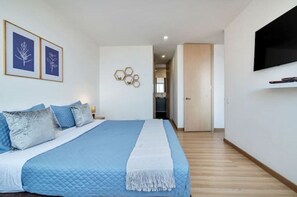 Une chambre avec un grand lit, un téléviseur fixé au mur et des reproductions botaniques encadrées accrochées au mur.