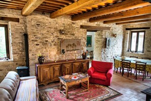 Una habitación rústica con paredes de piedra, techo de madera, un sillón rojo, una mesa de madera y un comedor con mesa y sillas.