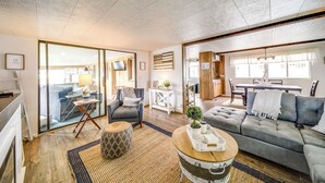 A spacious living room with a grey sofa, a wooden coffee table, and a patterned ottoman. There is a television mounted on the wall and a small side table with a lamp. - Seven Bays Vacation Rental on Lake Roosevelt! (Seven Bays)