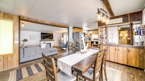 A spacious living area with a wooden dining table, chairs, and a sofa. There is a kitchen area with wooden cabinets and a countertop. - Seven Bays Vacation Rental on Lake Roosevelt! (Seven Bays)