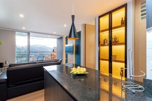A modern kitchen with a central island, a black pendant light, and a view of the city through large windows.