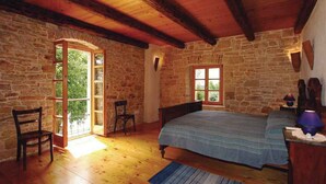 Un dormitorio rústico con paredes de piedra, vigas de madera, una cama, una silla y una ventana.