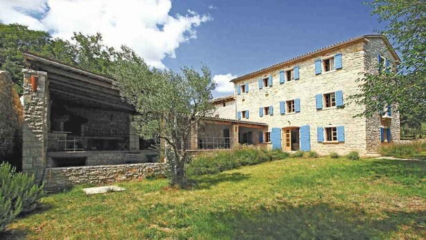 Un edificio de piedra con fachada de piedra y contraventanas azules, rodeado de césped y árboles.