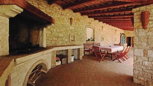 Un área de comedor al aire libre con paredes de piedra, piso de ladrillo, bancos de madera y una chimenea.