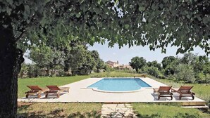 Piscina rectangular con solárium de piedra, rodeada de sillones de descanso.