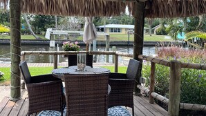 A wooden deck with a thatched roof, wicker furniture, and a glass table.