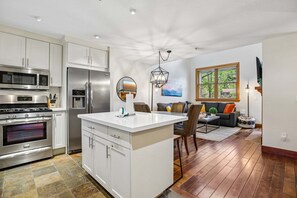 A modern kitchen with stainless steel appliances, a central island, and a dining area with a sofa and chairs.