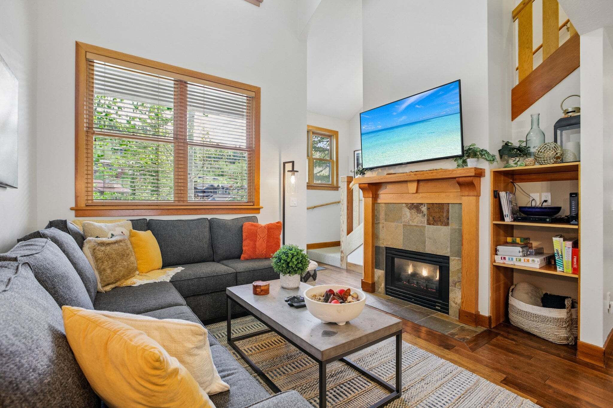 A living room with a sofa, coffee table, fireplace, TV, and large windows.
