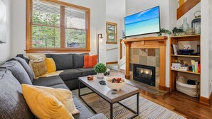 Una sala de estar con sofá, mesa de centro, chimenea, televisor y ventanas amplias.
