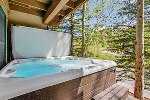 Een hottub met een houten terras, omringd door bomen en een helder uitzicht op een weg.