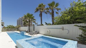Una piscina con borde de azulejos, sillas de descanso y palmeras.