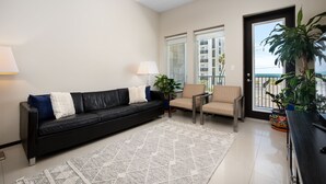 Una sala de estar moderna con un sofá de cuero negro, un sillón color beige, un tapete estampado y un ventilador de techo.
