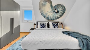 Una camera da letto moderna con un letto grande, un'opera d'arte a forma di cuore sulla parete e vista sul cielo attraverso una finestra.