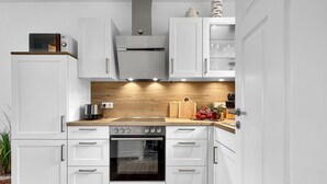Una cucina moderna con mobili bianchi, una schiena a parete in legno e un forno a incasso.