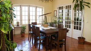 A dining area with a wooden table, chairs, a chandelier, potted plants, and a view through a glass door. - ITS A Room IN A Shared House (Caldas da Rainha)