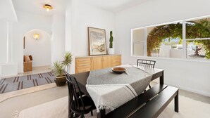 Un comedor con una mesa dispuesta para dos, un mueble de madera, una planta en maceta y un ventanal con vistas a la vegetación.