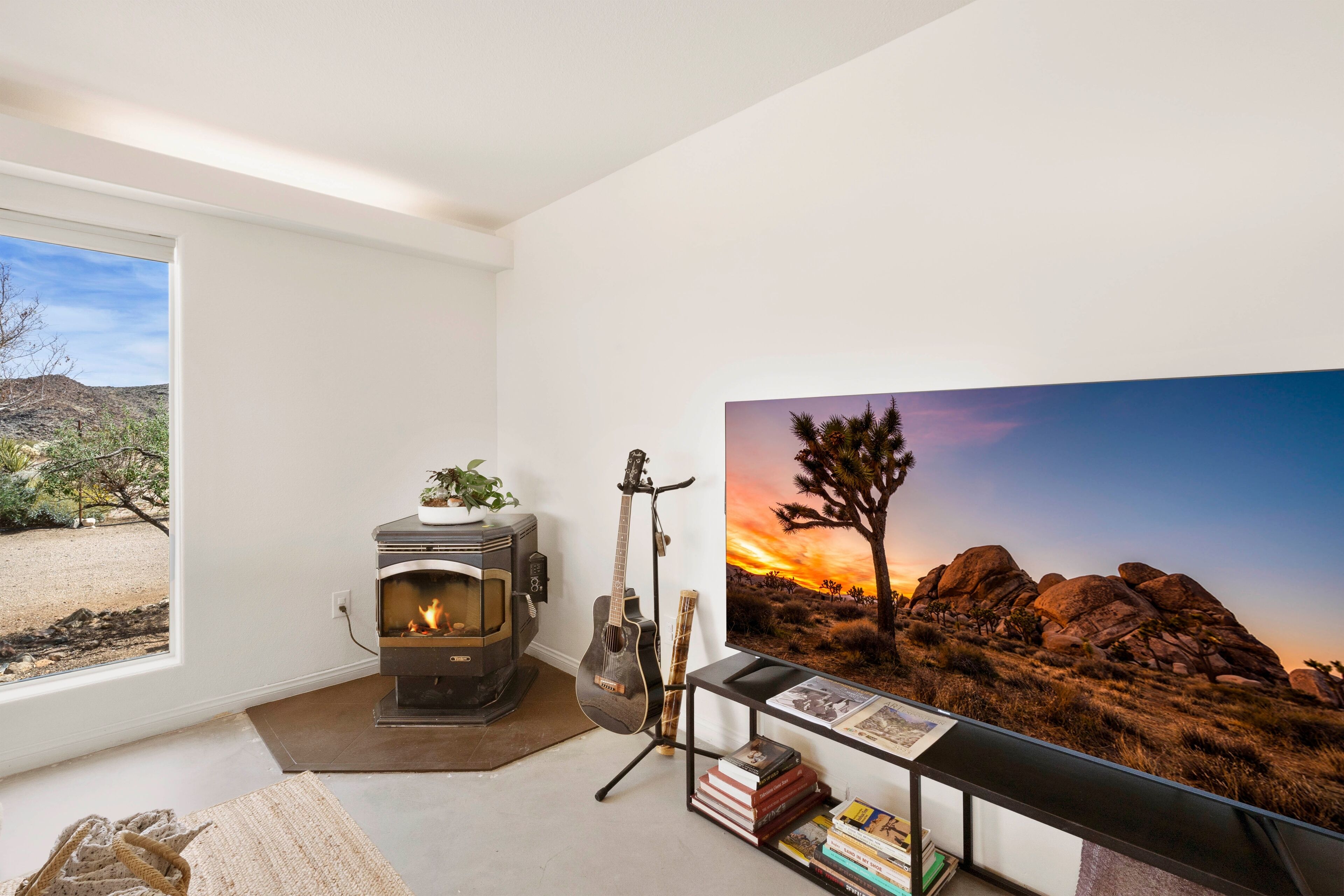 Una habitación con chimenea de leña, una guitarra, libros y un cuadro de paisaje desértico.