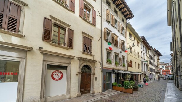 A cobblestone street with historic buildings, a restaurant sign, and outdoor seating with plants. - GuestHost - Cozy apartment of 55 sqm, able to accommodate up to 3 people, located on the third floor of a building without elevator. The location is great! In the center of Udine, overlooking Piazza Giacomo Matteotti; a few steps from the main points of  (Udine)