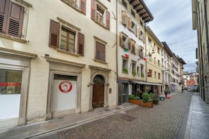 Une rue pavée bordée de bâtiments historiques, une enseigne de restaurant et des tables en plein air agrémentées de plantes.