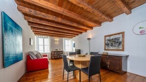 A spacious room with a wooden ceiling, a round dining table with chairs, a red sofa, and a cabinet. - GuestHost - Cozy apartment of 55 sqm, able to accommodate up to 3 people, located on the third floor of a building without elevator. The location is great! In the center of Udine, overlooking Piazza Giacomo Matteotti; a few steps from the main points of  (Udine)