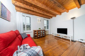 Una sala de estar con un sofá rojo, piso de madera, un televisor sobre un soporte blanco y techo de madera.