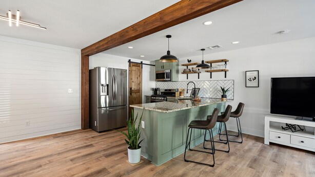 A modern kitchen with a large island, stainless steel appliances, and a TV.