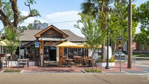 An outdoor cafe with tables and chairs under umbrellas, a wooden facade, and a sign reading "Welcome Our Happy Place".