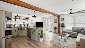 A modern kitchen with a central island, wooden beams, and a dining area with a sofa and coffee table.