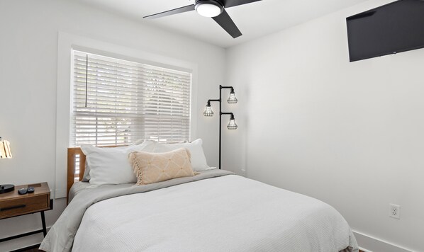 Une chambre à coucher avec un lit, une table de chevet, une lampe et un ventilateur de plafond.