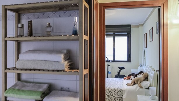 Une chambre avec un lit, une table de chevet, une fenêtre et une étagère où sont pliées des serviettes.