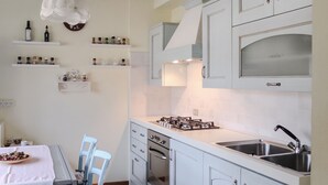 Une cuisine moderne avec des meubles blancs, une cuisinière à gaz, un évier à deux bacs et un coin repas comprenant une table et des chaises.