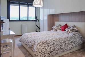A bedroom with a bed, a desk, a chair, a radiator, and a window.