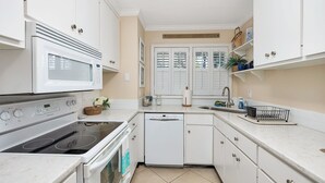 A compact kitchen with white cabinetry, a microwave, stove, and dishwasher. - Stones throw from shore!  Spacious multi-level townhome one row back from beach (St. Simons Island)