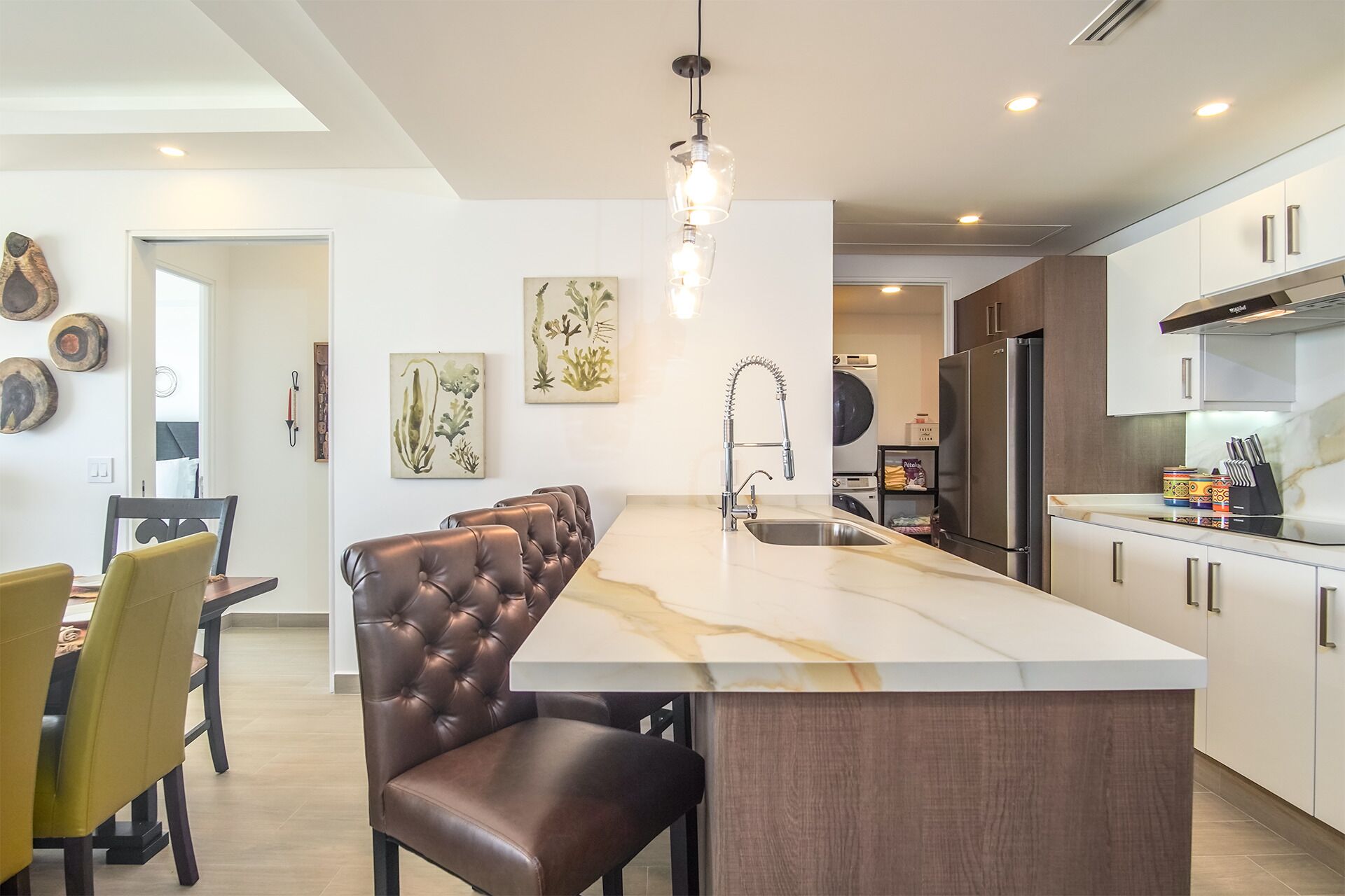 Una cocina moderna con una isla central, electrodomésticos de acero inoxidable y un comedor con sillas de cuero.