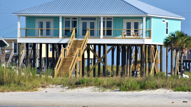 Una casa frente al mar de dos plantas con una terraza de madera y escaleras que suben al nivel superior.