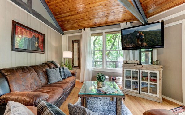 A cozy living room with a leather couch, a glass coffee table, and a television mounted on the wall.