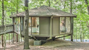 Una cabaña tipo casa del árbol con techo inclinado, ventanas amplias y una terraza.