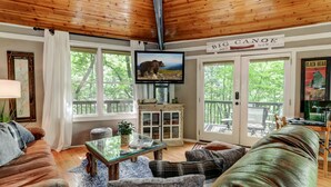 Una sala de estar acogedora con techo de madera, ventanas amplias, un televisor y un letrero que dice "BIG CANOE".