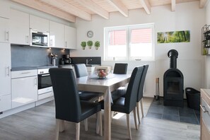Una cocina moderna con armarios blancos, horno empotrado y comedor con mesa de madera y sillas negras.