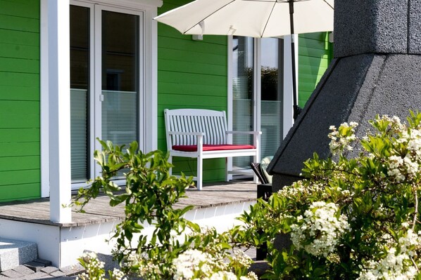 A green house with a white bench and a patio umbrella.