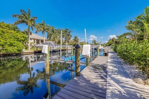 A marina with boats docked, a wooden walkway, and lush greenery.