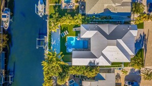 An aerial view of a modern house with a swimming pool, a boat dock, and a well-maintained garden.
