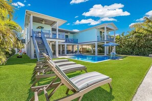 A modern two-story house with a swimming pool, a covered patio, and a well-maintained lawn.