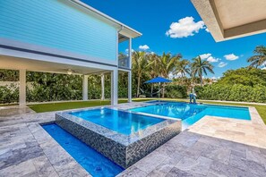 A modern house with a swimming pool, a covered patio, and lush greenery. - Manatee Lookout: Canal Front, Pool, Spa, Dock, Putting Green by Anna Maria Life Vacation Rentals (Anna Maria)